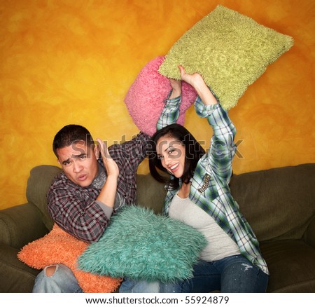 Hispanic couple on couch play fighting with pillows