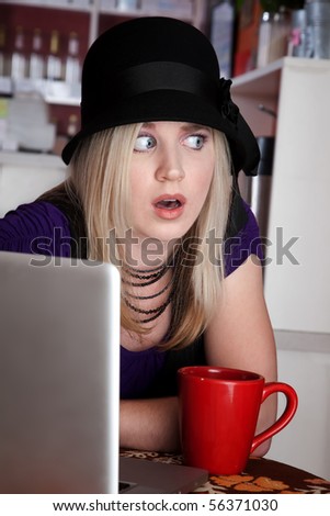 Blond woman looking surprised with laptop and mug at a cafe