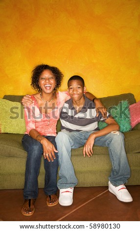 Good-looking single-parent mom and son sitting on sofa laughing
