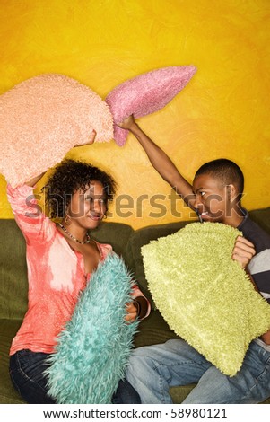 Woman and teen boy have pillow fight on green sofa
