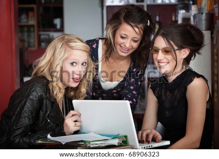 Three young college students laughing while looking at computer in a coffee house