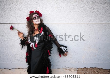 Woman in makeup for All Souls Day stands alongside a wall with red roses