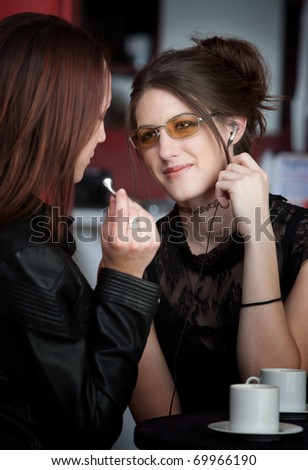 Two young teen friends sharing earphones in a cafe