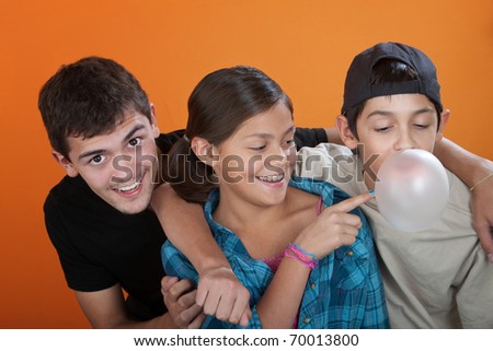 Young girl touching bubble from her brothers chewing gum on orange background