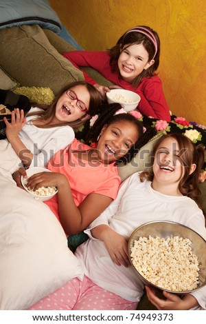 Four happy little girls on a couch eat popcorn