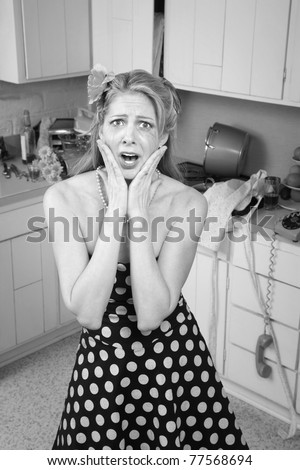Shocked Caucasian woman in messy retro-style kitchen with hands on face