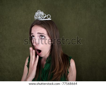 Young woman with crown on green background yawns
