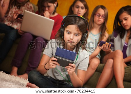 Wide-eyed little girl with headphones and game console with friends