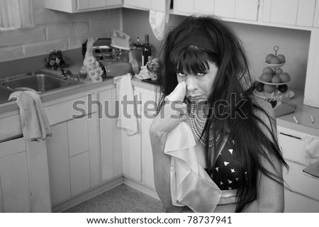 Weeping woman in a kitchen wipes tears using napkin