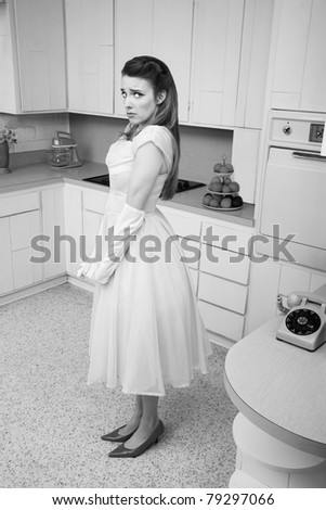 Unhappy young Caucasian woman stands alone by a phone in a retro-style kitchen