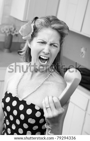 Woman in polka-dot dress yells at phone in kitchen