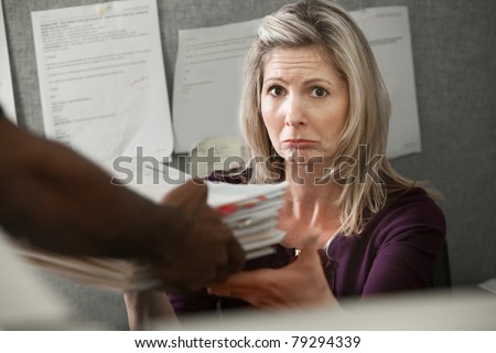 Unhappy Caucasian worker given a stack of files at a cubicle