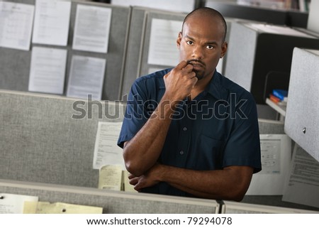 Serious African-American man with his hand on chin stands in his office cubicle