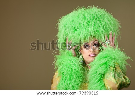 Serious drag queen holds wig on green background