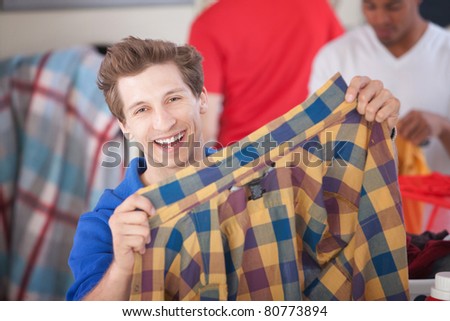 Grinning man holds a plaided shirt in laundromat