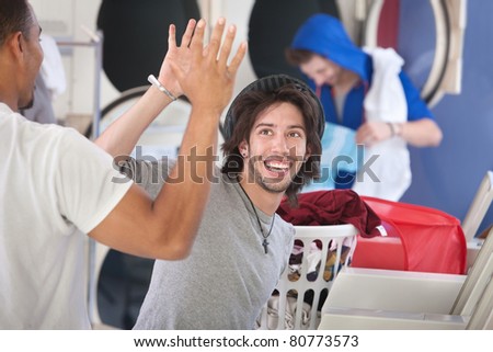 Two happy young friends high five in the laundromat