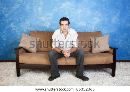 Bored young Caucasian man with hands clasped relaxes on sofa