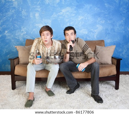 Two young Caucasian friends with drink cans and popcorn watch television