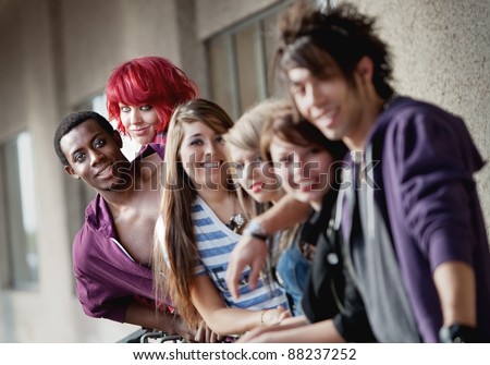 Punk rock looking teens smile at the camera as the camera focuses on the back two individuals.