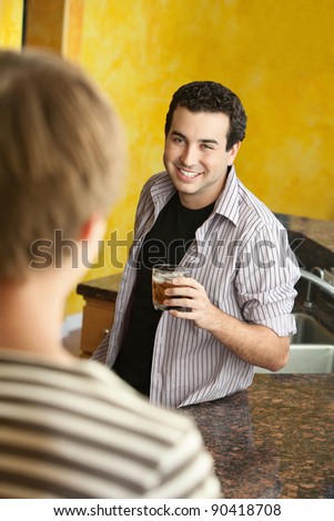 Happy young Caucasian man enjoys a drink with friend in kitchen