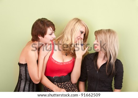 Three beautiful young teen girls share gossip with each other in front of a green wall.