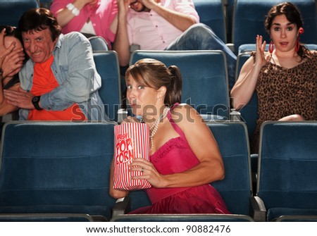 Woman snacks on popcorn with group seated in theater