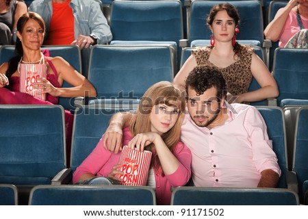 Young romantic couple with popcorn bag at movie in theater