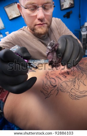 Bearded Caucasian tattooist creates a tattoo on a woman\'s back