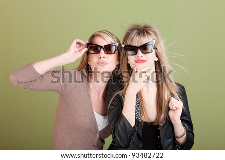 Mom and daughter with sunglasses over green background gaze