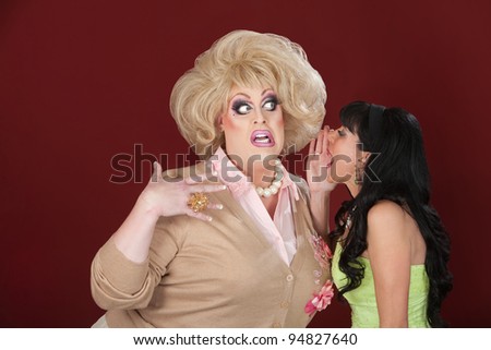 Retro-styled lady whispers secret to a surprised drag queen