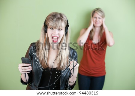 Excited retro-styled woman sings out loud with annoyed mom behind her