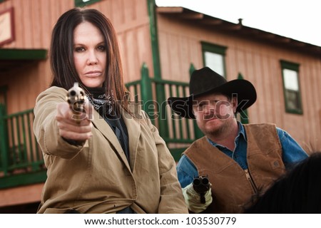 Pretty woman and partner aim guns in old west town