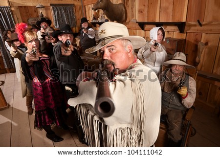 Tough old west desperado and group point their weapons in a bar