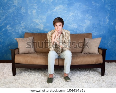 Cute young man sitting in middle of sofa indoors