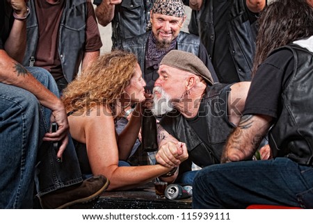 Two biker gang lovers kiss while arm wrestling