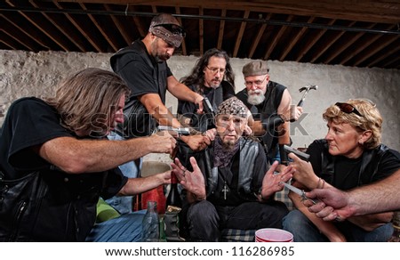 Group of bikers in leather hold up sitting man