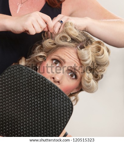 Nervous female holding mirror with hair stylist working