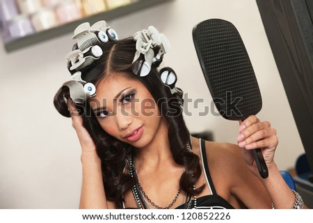 Beautiful Vietnamese lady with hair curlers and mirror
