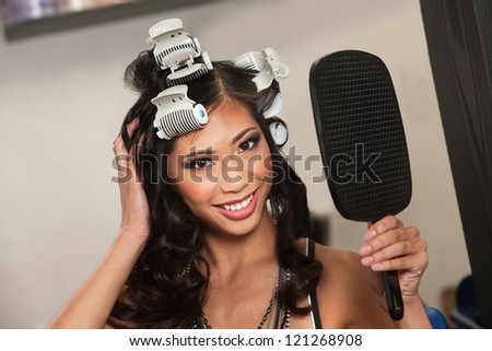 Smiling young woman in curlers holding mirror