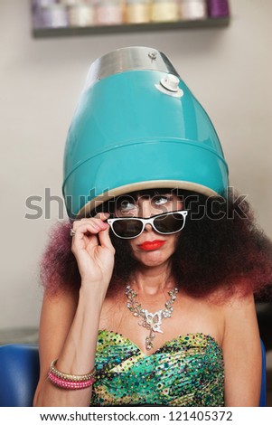 Pouting lady with frizzy hair sitting under hair dryer