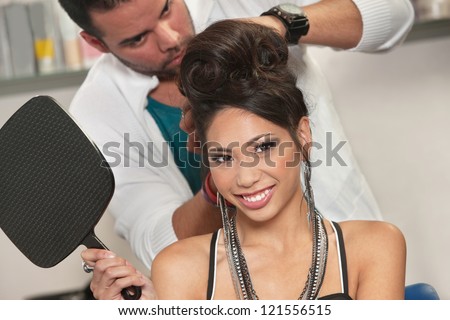Vietnamese female holding mirror with hairdresser working behind her