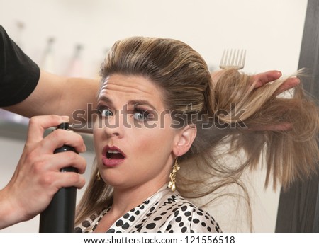 Pretty woman is startled by stylist using hair spray