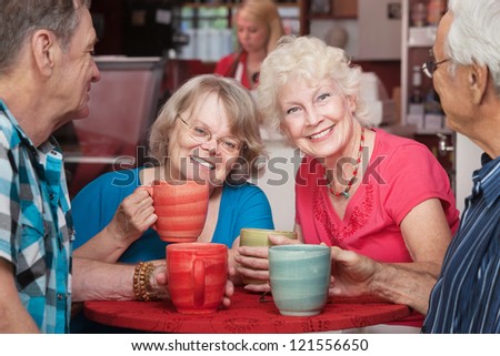 Senior female friends smiling at cafe with group