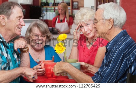 Woman holding forehead as friends laugh at the table