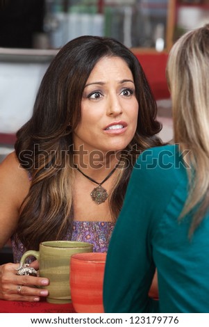 Concerned Hispanic woman looking at her friend in cafe