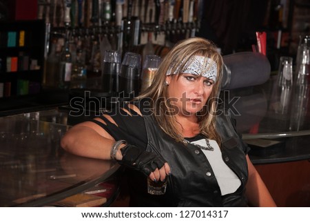Grumpy biker gang lady holding her drink at a bar