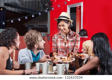 Smiling Asian woman sharing pizza slices with friends at food truck