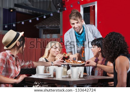 Smiling hipster serving pizza to group outside