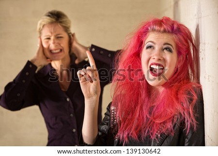 Woman covering ears while woman in pink hair sings
