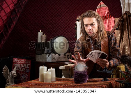Male fortune teller with tarot cards waving hand over crystal ball